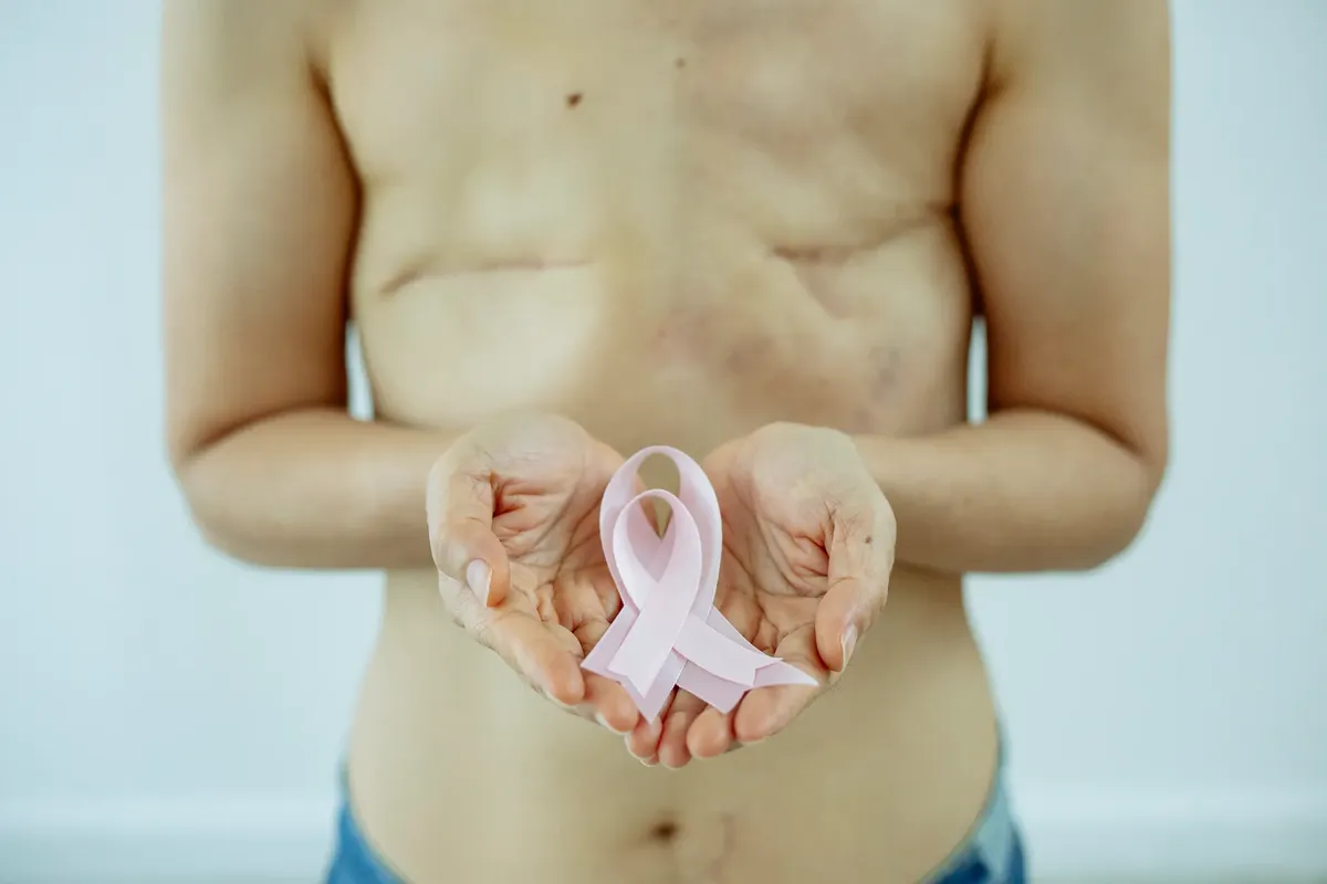 Crop unrecognizable topless woman with scars on breast after operation showing pink ribbon as sign of Breast Cancer day in light studio